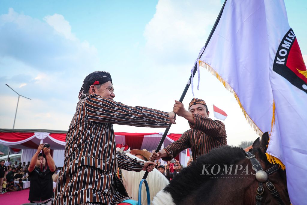 Ketua KPU Nganjuk Pujiono (kanan) menyerahkan menyerahkan bendera KPU kepada Ketua KPU Magetan Fahrudin (kiri) dalam Kirab Pemilu 2024 di Taman Refugia, Magetan, Jawa Timur, Rabu (25/10/2023). 