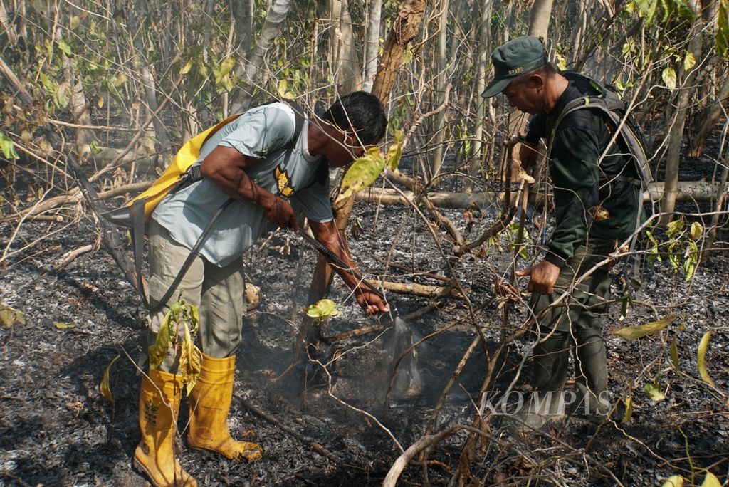 Petugas Manggala Agni menyemburkan air yang disimpan dalam sebuah tas, Jumat (27/9/2019), untuk memadamkan kebakaran lahan hutan Taman Wisata Alam Batuputih, Bitung, Sulawesi Utara. Kebakaran itu menyebabkan seekor rusa mati.