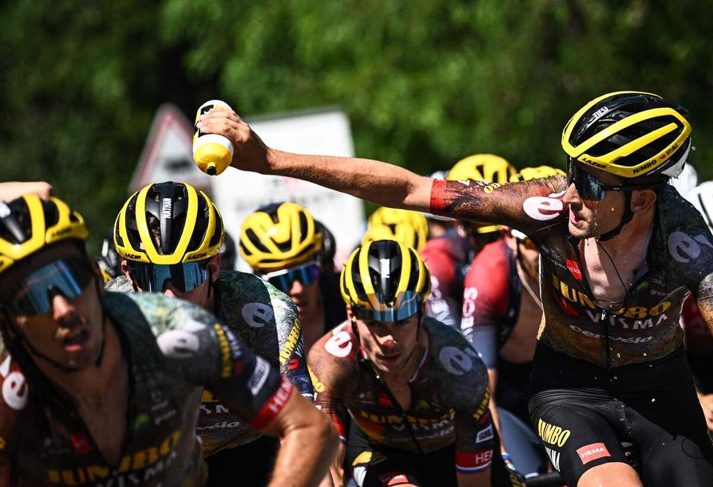 Pebalap Jumbo-Visma asal Belgia, Tiesj Benoot (kanan), menuangkan air ke rekan timnya untuk mendinginkan badan saat etape ke-12 Tour de France, 14 Juli 2022. 