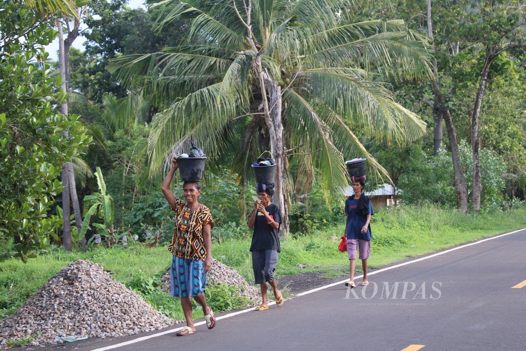 Ibu-ibu membawa cucian berjalan kaki menyusuri jalan Trans-Flores tepatnya di Desa Konga, Kecamatan Titehena, Kabupaten Flores Timur, Nusa Tenggara Timur, Kamis (18/1/2024) petang. 