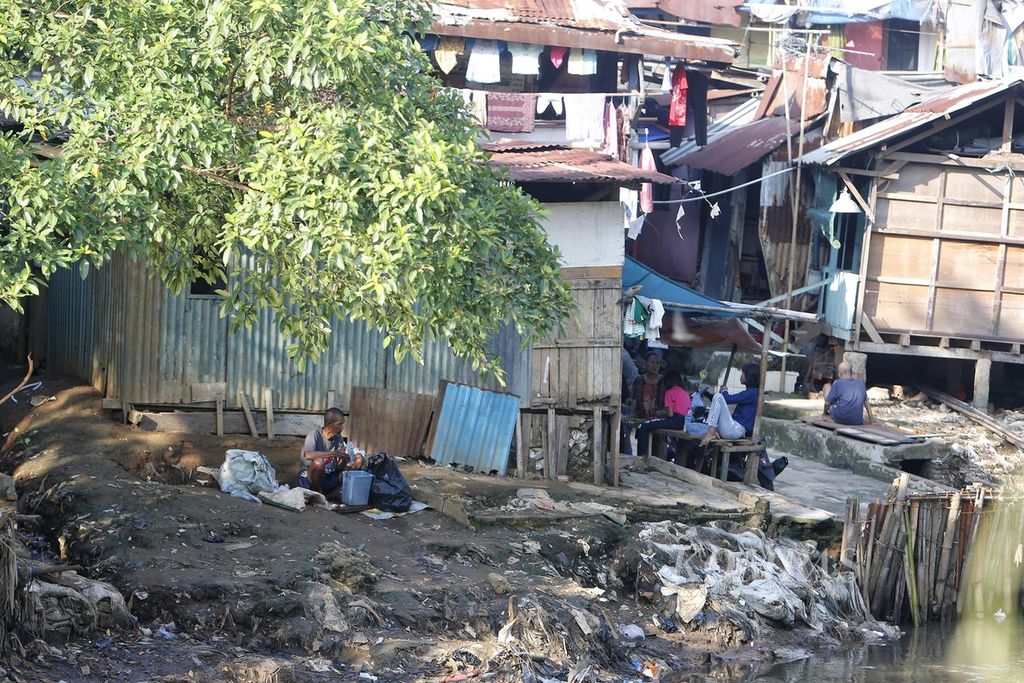 Warga beraktivitas di depan deretan hunian semipermanen yang berdiri di tepian Kali Ciliwung yang melintasi kawasan Bidara Cina, Jatinegara, Jakarta Timur, Senin (10/7/2023). Pemerintah menargetkan kemiskinan ekstrem turun menjadi 0 persen pada tahun 2024. 