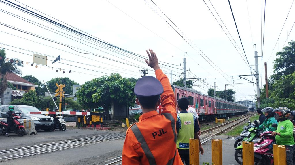 Harwanto (27), penjaga jalan lintasan kereta api, melambaikan tangan ke kereta yang sedang melintas saat tengah mengatur lalu lintas di Jalan Jembatan Besi Raya, Kecamatan Tambora, Jakarta Barat, Rabu (8/2/2023).