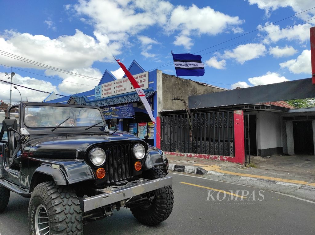 Sebuah mobil berjalan melintasi sebuah bendera pendukung PSIM Mataram yang terpasang di pagar salah satu restoran di Jalan Mayjen Bambang Sugeng, Danurejan, Kota Yogyakarta, Daerah Istimewa Yogyakarta, Senin (8/8/2022). Brajamusti, salah satu kelompok suporter PSIM, membuat kampanye #BIRUKANDIY untuk pemasangan bendera itu sejak 2019.