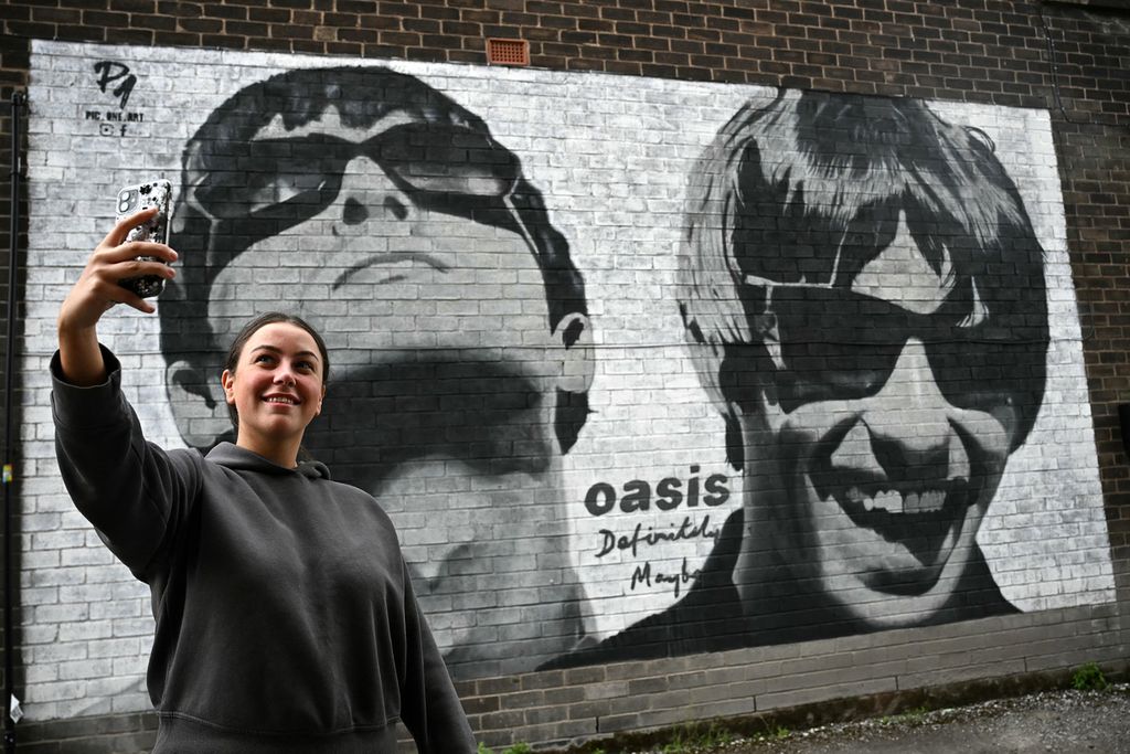 Penggemar, Emily McShane, berswafoto dengan karya seni jalanan baru yang menggambarkan Liam dan Noel Gallagher dari Oasis, yang dibuat seniman jalanan di Manchester, Inggris, pada 27 Agustus 2024.