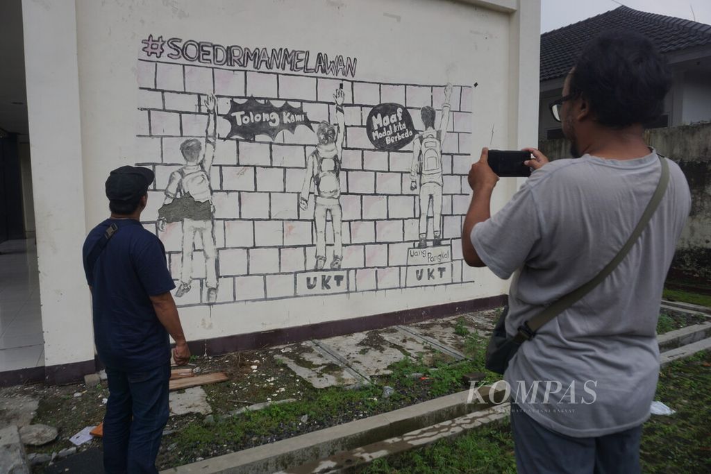 Mural atau lukisan dinding terkait uang kuliah tunggal tampak di dinding bangunan kompleks Pusat Kegiatan Mahasiswa Universitas Jenderal Soedirman, Purwokerto, Banyumas, Jawa Tengah, Kamis (25/4/2024).