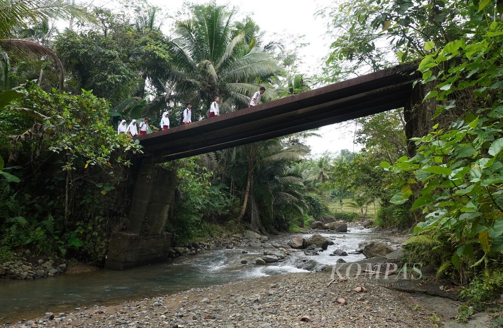 Siswa berjalan melewati jembatan yang rusak akibat tanah bergerak menuju Madrasah Ibtidaiyah Pasawahan, Kecamatan Banjaranyar, Kabupaten Ciamis, Jawa Barat, Selasa (19/7/2022). Mayoritas siswa berjalan kaki menuju sekolah selama lebih kurang 20 menit.