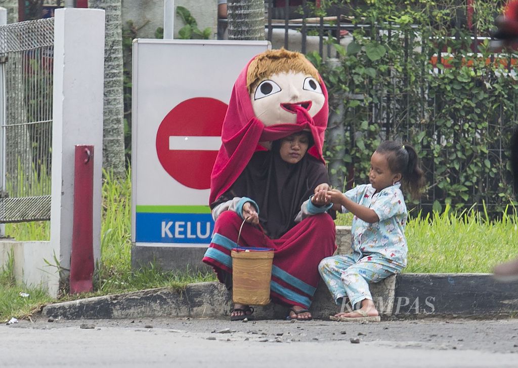 Seorang ibu berpakaian badut bersama anaknya mengharapkan sedekah dari para pengguna jalan di kawasan Cinere, Depok, Jawa Barat (1/4/2022). Badan Pusat Statistik (BPS) mencatat, per September 2021, masih ada 26,5 juta orang miskin di Indonesia yang memerlukan bantuan dan sedekah.