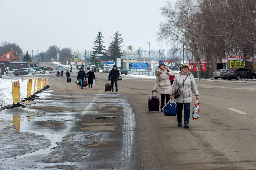 Warga menenteng koper saat berjalan ke sisi perbatasan Rusia di pos pemeriksaan perbatasan Ukraina-Rusia, sekitar 40 kilometer dari kota terbesar kedua di Ukraina, Kharkiv, 16 Februari 2022.  