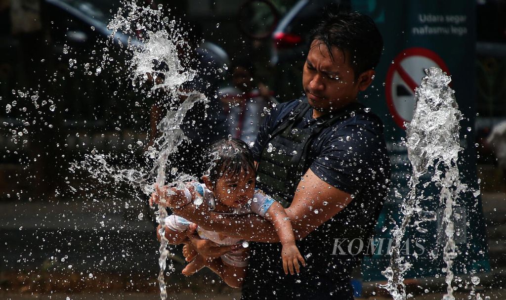 Warga menggendong anak balitanya untuk bermain air mancur di Taman Gandaria Tengah, Kramat Pela, Kebayoran Baru, Jakarta Selatan, Minggu (1/10/2023). Air mancur yang terdapat di sejumlah taman kota ini menjadi alternatif wisata murah. 