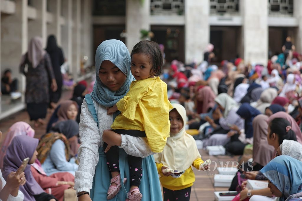 Seorang remaja menggendong anak saat buka bersama di Masjid Istiqlal, Jakarta, Selasa (12/3/2024). Tugas perawatan yang dibebankan pada anak perempuan acapkali membuat mereka lebih sedikit waktu untuk mengakses pendidikan dan kesempatan kerja.   