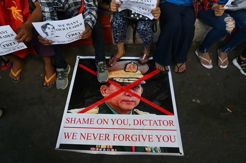 Pengunjuk rasa duduk di dekat poster bergambar wajah pemimpin junta militer Myanmar, MIn Aung Hlain yang telah disilang dengan pita warna merah di Yangon pada 11 Februari 2021.