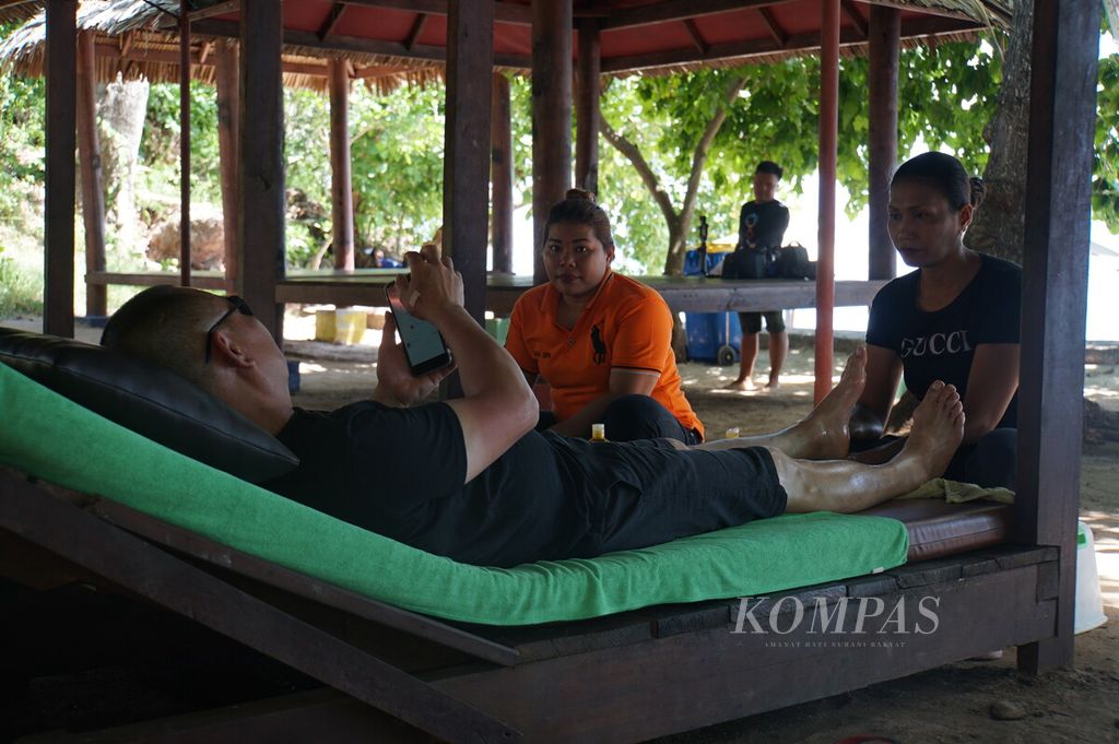 Linda Amar memijat kaki seorang wisatawan asal China di tepi pantai Pulau Gangga, Minahasa Utara, Sulawesi Utara, Jumat (31/1/2020). Linda belum tahu apakah ia akan tetap bekerja selama penerbangan dari China ke Manado ditutup sementara.