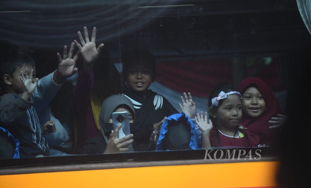 Peserta mudik bareng gratis 2024 melambaikan tangan saat meninggalkan depan kantor Dinas Perhubungan Jawa Timur, Minggu (7/4/2024). 