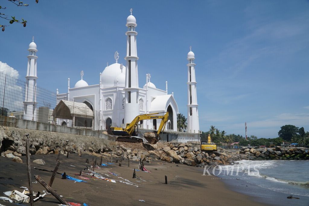 Pekerja sedang menyusun batu pemecah ombak menggunakan alat berat untuk melindungi masjid yang diproyeksi menjadi ikon wisata halal di Pantai Muaro Padang, Sumatera Barat, Senin (5/8/2019).