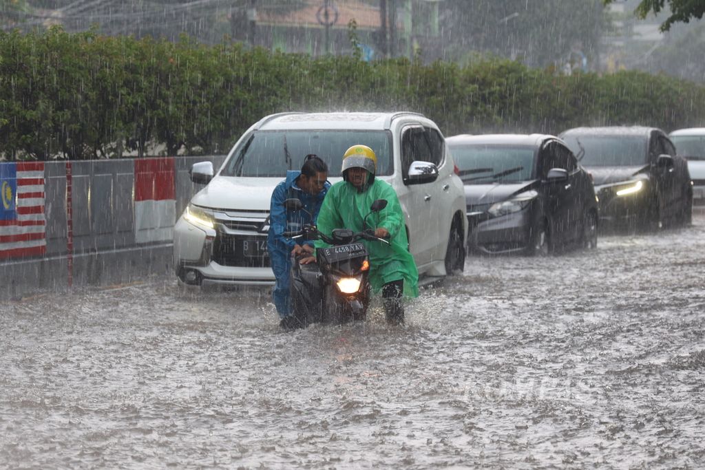 Petugas Penanganan Prasarana dan Sarana Umum mendorong motor yang mogok akibat tidak mampu melewati genangan air setinggi setengah meter saat hujan deras mengguyur di kawasan Gandaria, Jakarta Selatan, Sabtu (6/1/2024). 