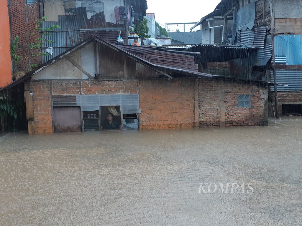 Seorang warga bertahan di dalam rumah yang telah kebanjiran air dari sungai tepat di hadapannya, Jumat (27/1/2023), di Kecamatan Singkil, Manado, Sulawesi Utara. Hujan deras yang mengguyur sejak dini hingga sore hari menyebabkan banjir dan tanah longsor di 23 kelurahan yang tersebar di delapan kecamatan.