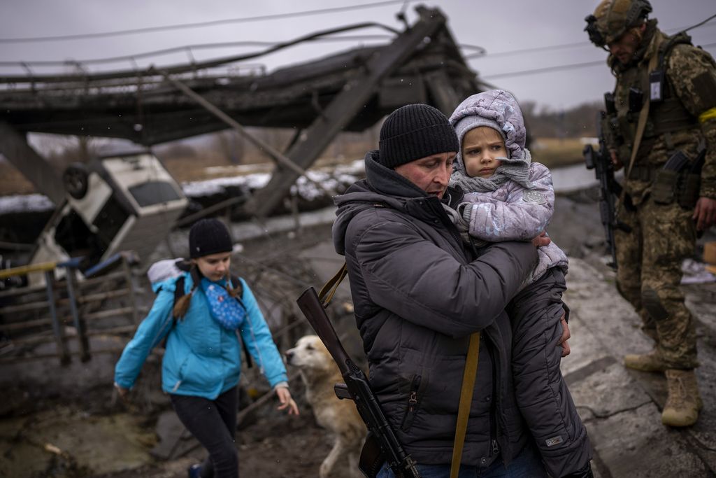 Anggota milisi lokal, Valeri (37), menggendong seorang anak saat ia membantu satu keluarga yang mengungsi melewati sebuah jembatan yang hancur akibat gempuran artileri di pinggiran Kiev, Ukraina, Rabu (2/3/2022). 
