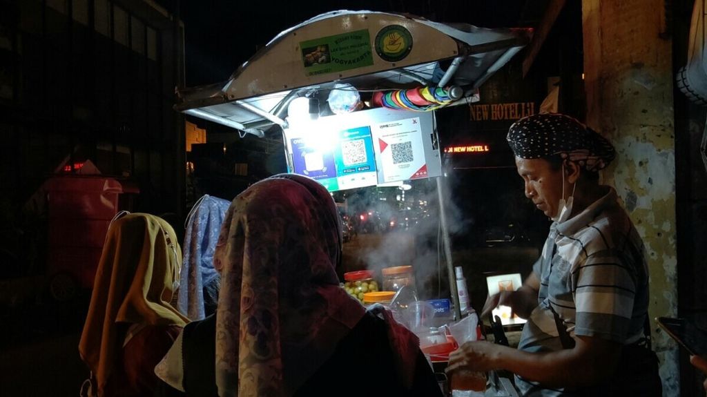 Kaswadi (42) melayani pembeli ronde yang berlokasi di Jalan Dagen, Gedong Tengen, Kota Yogyakarta (9/1/2022). Tampak kode QR untuk mengakomodasi pembayaran elektronik dengan dompet digital maupun mobile banking. 