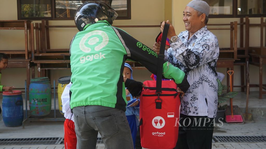 Seorang guru menerima kiriman paket makanan dari pengemudi Gojek dalam uji coba program makan bergizi gratis di SD Negeri Tugu 120 Surakarta, Kota Surakarta, Jawa Tengah, Kamis (25/7/2024). 