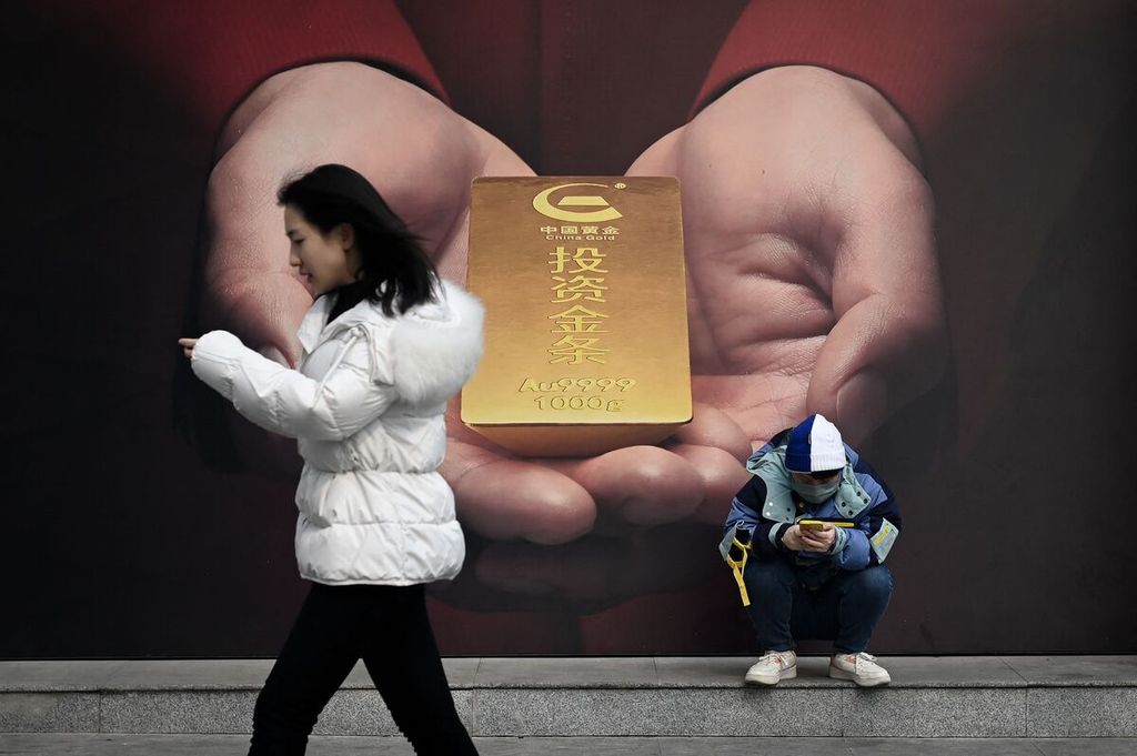 Seorang perempuan berjalan di depan poster bergambar emas di sebuah ruas jalan di Beijing, China, 27 Februari 2024. 