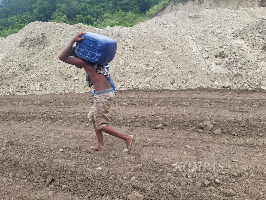 Seorang remaja memikul jeriken berisi bahan bakar melewati lokasi longsor di Kelurahan Takari, Kabupaten Kupang, Nusa Tenggara Timur, pada Senin (20/2/2023). Longsor menghambat mobilisasi logistik, termasuk bahan bakar.