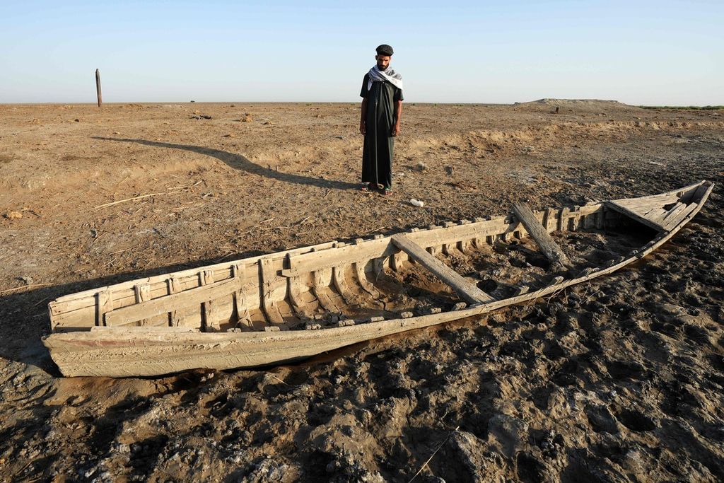 Seorang warga Irak melihat sebuah perahu yang terdampar di pesisir rawa Chibayish, Irak yang telah mengering. Foto diambil pada Minggu (25/6/2023).