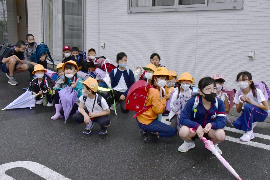 Siswa sekolah dasar berlindung di dekat sebuah bangunan saat menuju sekolah tak lama setelah muncul peringatan dan laporan peluncuran rudal balistik Korea Utara di Misawa, Prefektur Aomori, Jepang, 4 Oktober 2022. 