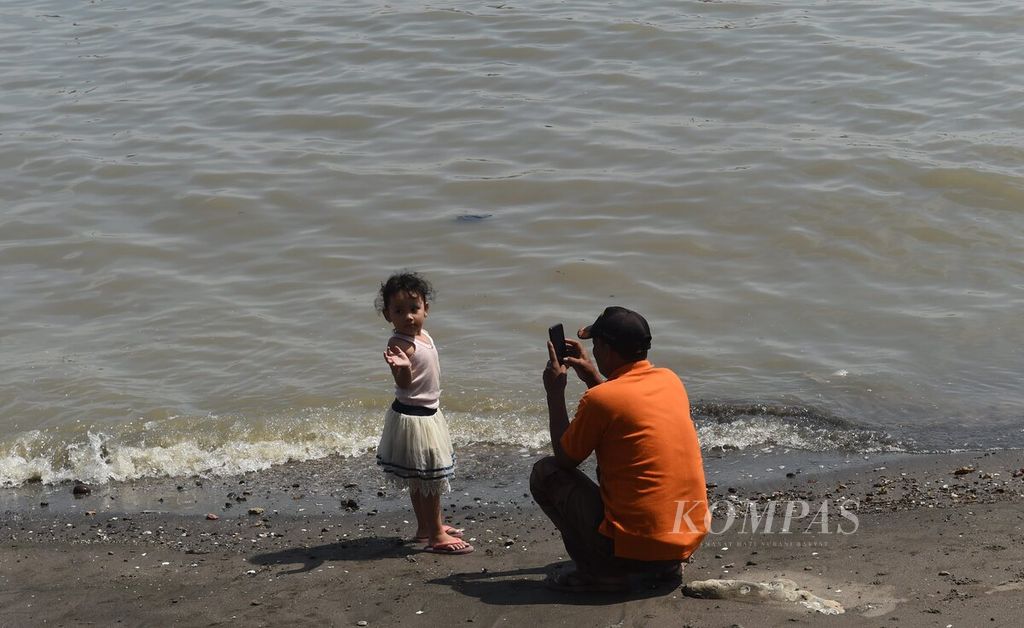 Warga berfoto di kawasan pesisir saat cuaca panas, di Kota Surabaya, Jawa Timur, Selasa (27/9/2022).