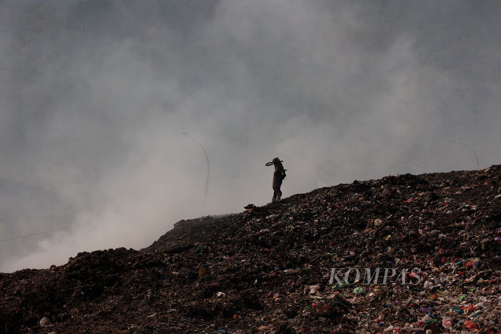 Warga berjalan di atas tumpukan sampah dengan latar belakang kepulan asap yang masih membubung di Tempat Pembuangan Akhir Jatibarang, Kota Semarang, Jawa Tengah, Senin (9/10/2023). 