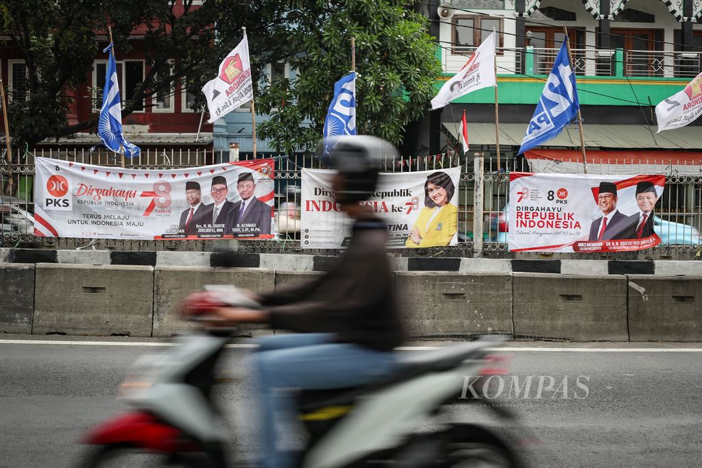Pengendara sepeda motor melintasi deretan spanduk dan bendera partai politik di Jalan Mampang Prapatan Raya, Jakarta Selatan, Minggu (20/8/2023). 