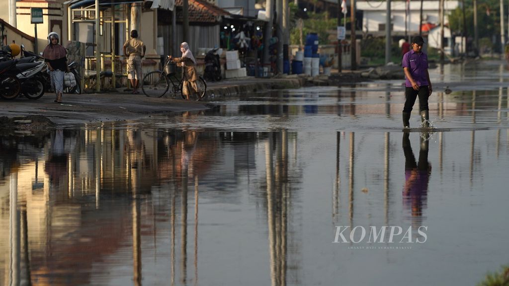 Warga melintasi limpasan air laut di Jalan WR Supratman, Pekalongan Utara, Jawa Tengah, Selasa (20/12/2022). Selain hujan intensitas tinggi dan rob, wilayah pesisir utara Jawa setiap tahun juga selalu terancam dengan semakin meningkatnya tinggi muka air laut.  