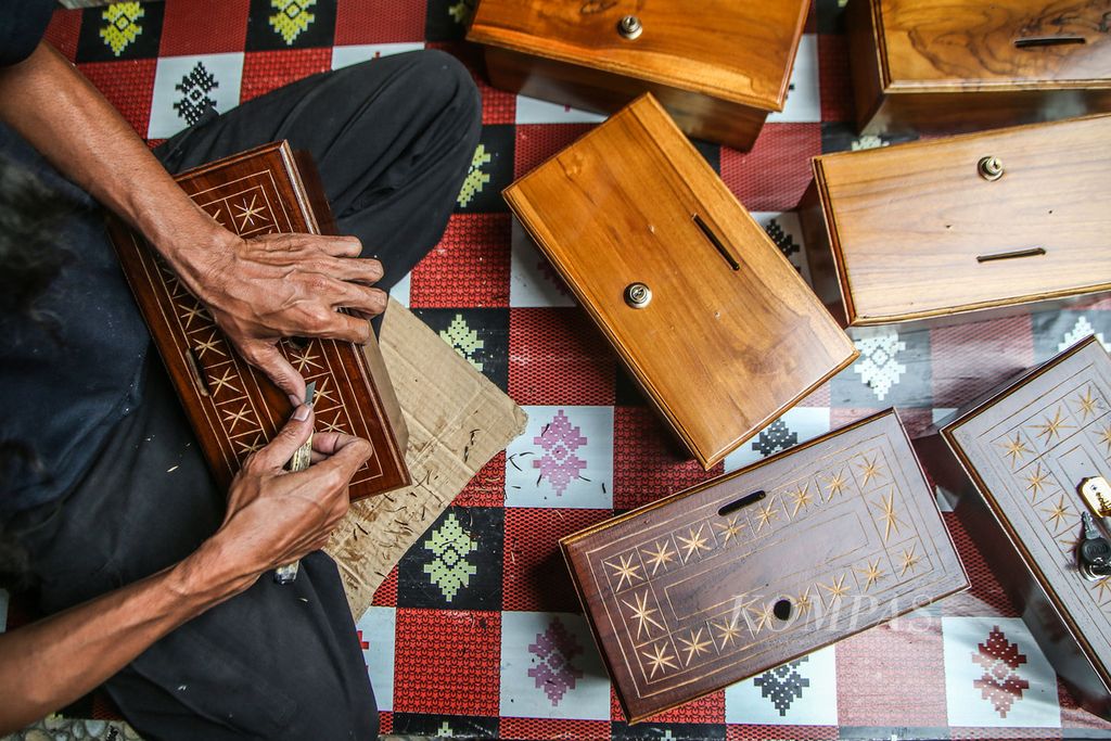 Seno menyelesaikan ukiran kotak amal berbahan kayu jati di Galeri Cemolek, Curug, Depok, Jawa Barat, Minggu (18/4/2021). Kotak amal itu dijual mulai Rp 100.000 melalui platform e-dagang ke seluruh Nusantara. 