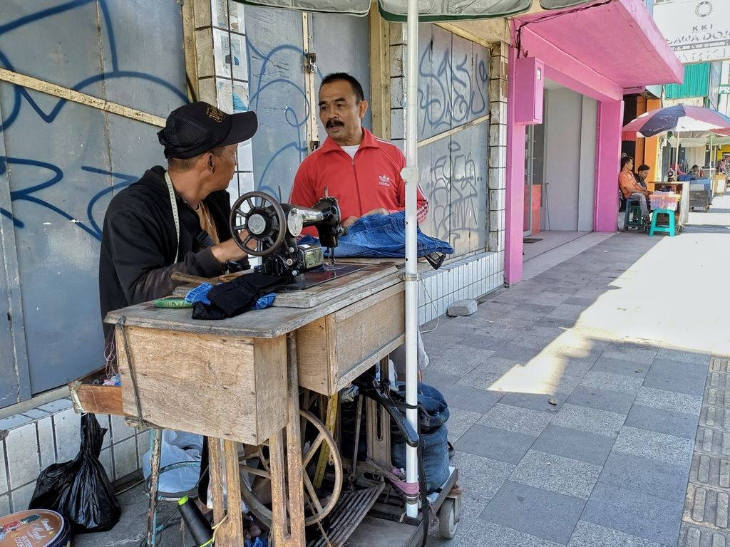 Agus Sopian (45) berbincang dengan salah satu konsumennya di lapak tepi jalan Pasar Kosambi Kota Bandung, Jawa Barat, Minggu (24/3/2024).