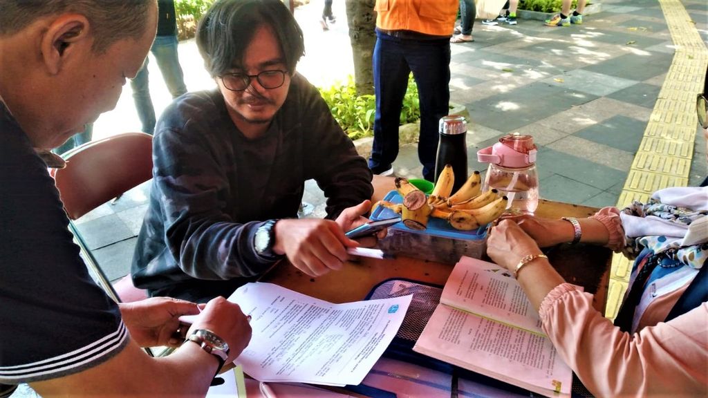 Muhammad Bohari (27), pelanggar yang membuang puntung rokok sembarangan, duduk bersama temannya di sekitaran Hotel Indonesia Kempinski. Bohari sedang melakukan pembayaran denda langsung di posko penindakan DLH DKI Jakarta, Bundaran HI, Jakarta Pusat, pada Minggu (23/10/2022).