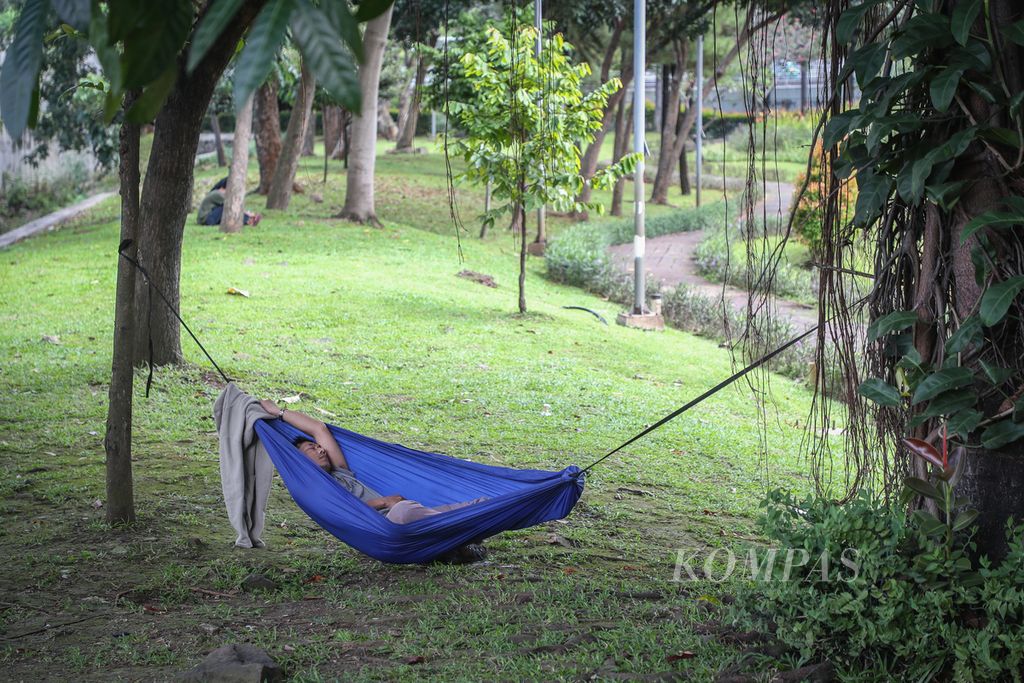 Warga tidur menggunakan <i>hammock</i> atau tempat tidur gantung di Taman Cattleya, Jakarta Barat, Jumat (12/5/2023). Taman Cattleya menjadi salah satu tempat favorit warga Jakarta untuk bersantai dan menikmati udara sejuk di tengah hiruk pikuk kota. 