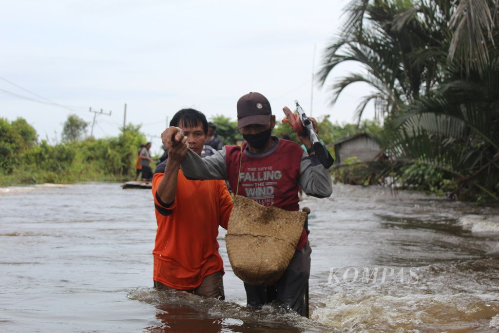 Warga Desa Lembeng, Kabupaten Barito Selatan, Kalimantan Tengah, membantu warga lainnya yang ingin melintas di tengah banjir yang melanda jalur Trans-Kalimantan, Kamis (25/1/2024).