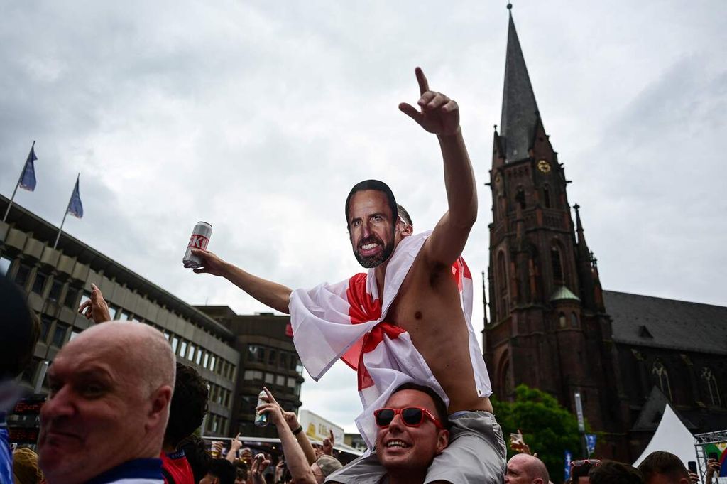 Seorang suporter Inggris memakai topeng wajah Pelatih Inggris Gareth Southgate berpawai di Heinrich-Koenig Platz, Gelsenkirchen, Jerman, Minggu (30/6/2024). 