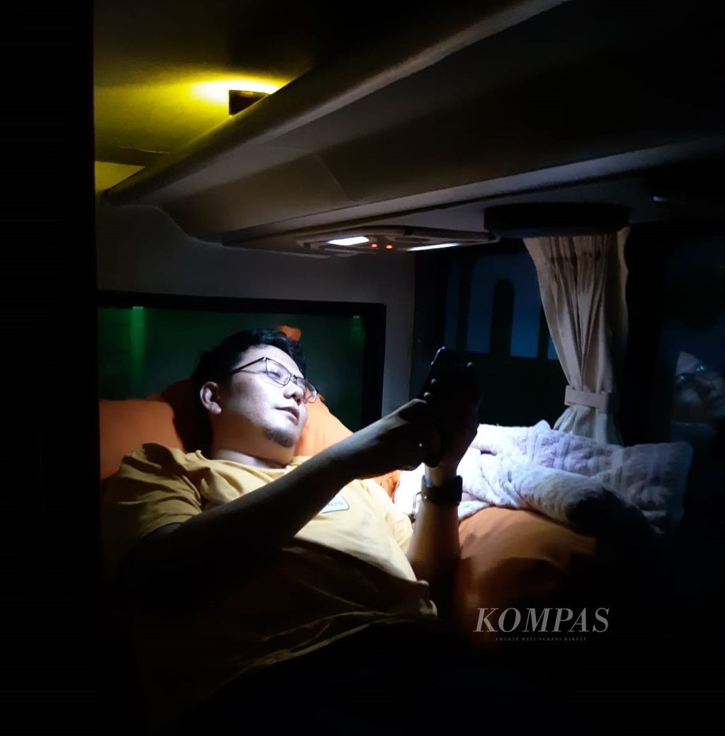 Seorang penumpang bus <i>sleeper</i> PO Harapan Jaya rute Jakarta-Tulungagung, Jawa Timur, pada Kamis (7/12/2023) malam, sedang beristirahat di kabin yang menyediakan fasilitas kursi yang bisa disetel untuk tidur dengan nyaman.
