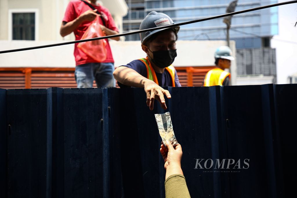 Pekerja menerima uang kembalian dari balik pagar proyek properti di kawasan Kebon Melati, Tanah Abang, Jakarta Pusat, saat jam istirahat, Selasa (28/9/2021). 