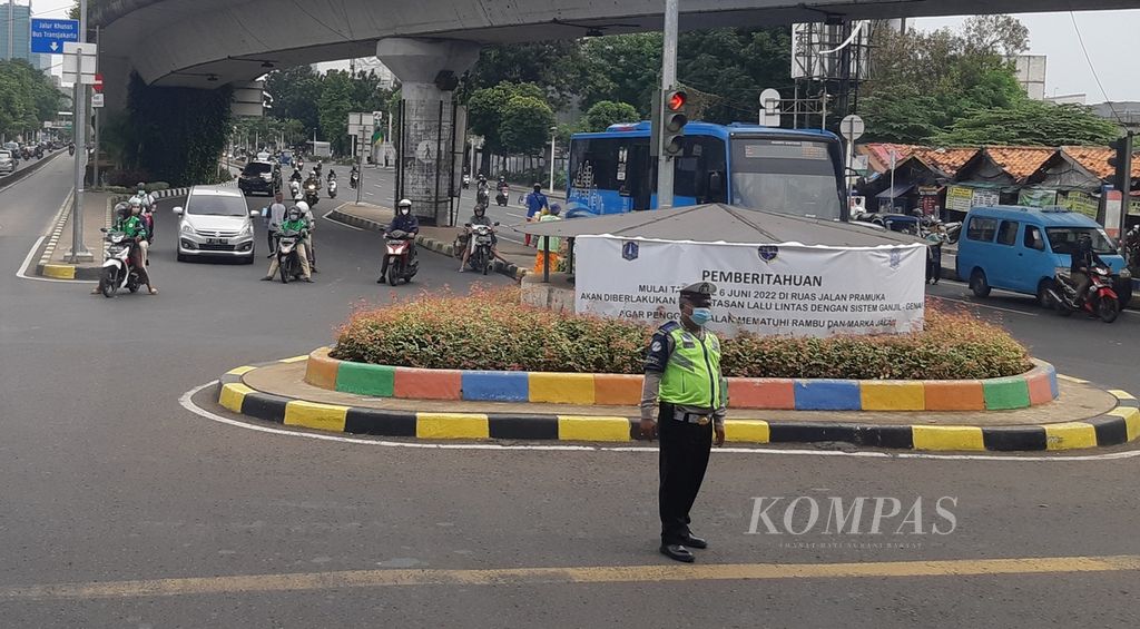 Polisi berdiri di depan poster pemberitahuan penerapan kembali sistem ganjil genap di Jalan Salemba Raya, Jakarta Pusat, Senin (13/6/2022). Polisi telah menerapkan sanksi bagi pelanggar aturan tersebut.