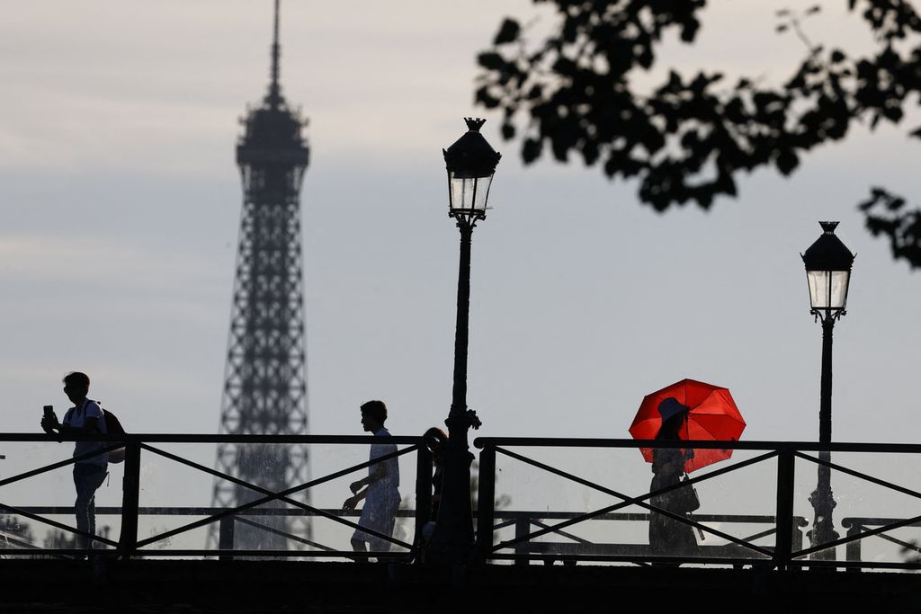 Orang-orang melintas di jembatan dengan latar belakang Menara Eiffel, di Paris, Perancis, Selasa (12/7/2022). 