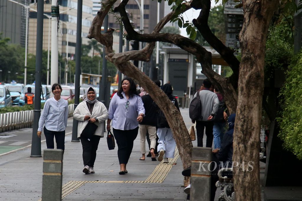 Pekerja kantor berjalan di trotoar Jalan MH Thamrin, Jakarta, saat jam isitrahat siang, Jumat (16/2/2024).