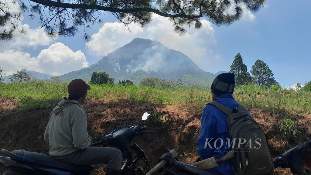 Dua warga tengah mengamati asap tebal yang mengepul dari hutan yang ada di lereng Gunung Panderman di Kota Batu, Jawa Timur, Rabu (22/11/2023). Sambaran petir diyakini menjadi penyebab kebakaran hutan di Panderman kali ini.
