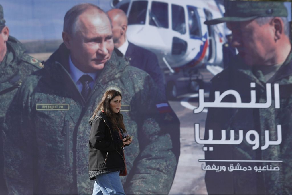 Seorang perempuan berjalan melewati sebuah billboard dengan gambar Presiden Rusia Vladimir Putin. BIllboard itu terpasang di pinggir sebauh jalan di Damaskus, Suriah pada Senin (7/3/2022). Tulisan dalam billboard itu terdapat tulisan dalam bahasa Arab yang berarti "Kemenangan untuk Rusia".