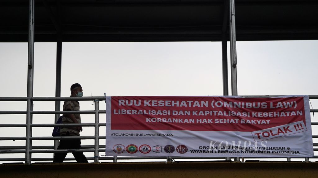 Warga melewati spanduk penolakan RUU Kesehatan di Tebet, Jakarta Selatan, Junat (25/11/2022). Rancangan Undang-Undang Kesehatan yang disusun dengan menghimpun sejumlah regulasi atau <i>omnibus law </i>masuk ke dalam Program Legislasi Nasional Prioritas tahun 2023. Namun, sampai saat ini penyusunan RUU ini tidak pernah melibatkan organisasi profesi kedokteran. 