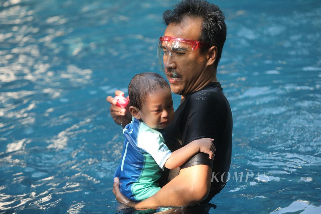Ayah menggendong bayinya saat berlatih renang dalam pelatihan khusus di sebuah kolam di kawasan Cempaka Putih, Jakarta, Sabtu (30/7/2022).