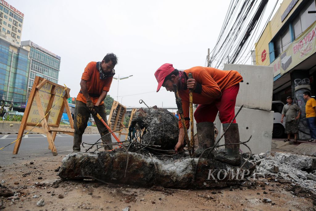 Dua pekerja memotong beton yang tertancap pada bongkahan galian perbaikan saluran air di Jalan Otista Raya, Jakarta Timur, Kamis (27/7/2023). Perbaikan saluran ini dikerjakan sejak pertengahan Juli 2023 dan diperkirakan selesai pertengahan Agustus 2023. Akibat perbaikan ini, akses masuk sejumlah toko harus dibantu papan kayu untuk menyeberangi galian. Laju kendaraan juga tersendat akibat perbaikan saluran ini. 