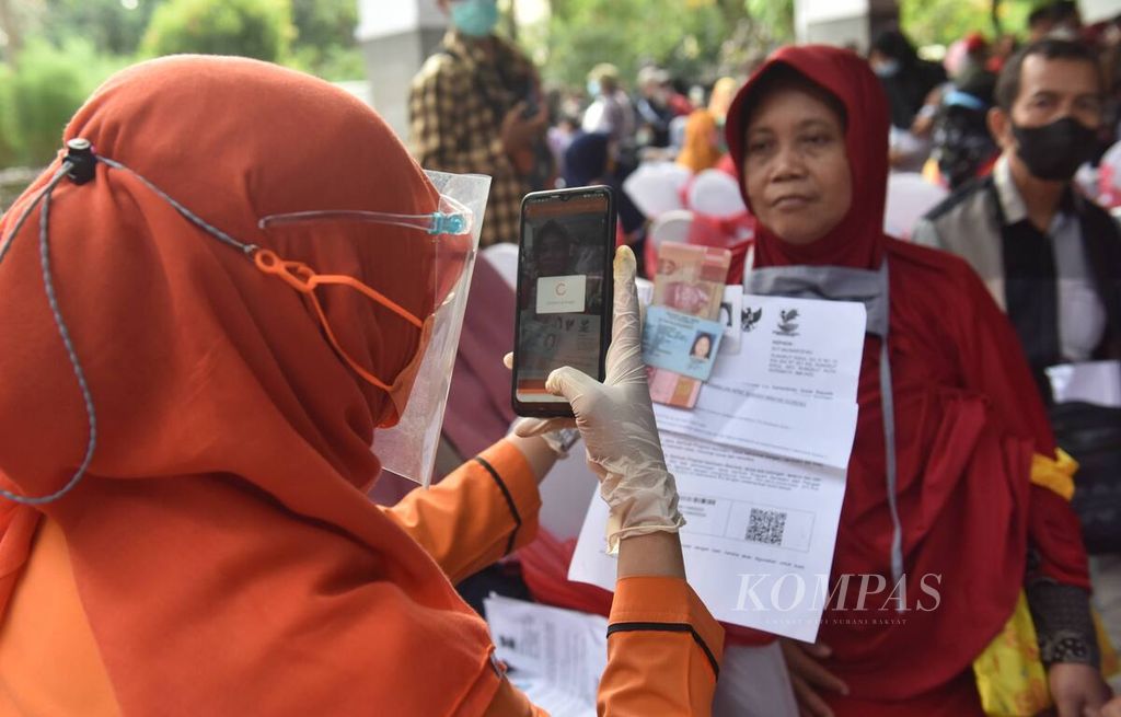 Petugas memotret warga yang akan menerima uang saat penyaluran bantuan Program Keluarga Harapan, Bantuan Pangan Non-Tunai, dan bantuan langsung tunai minyak goreng di Kantor Kecamatan Rungkut, Kota Surabaya, Jawa Timur, Sabtu (16/4/2022).