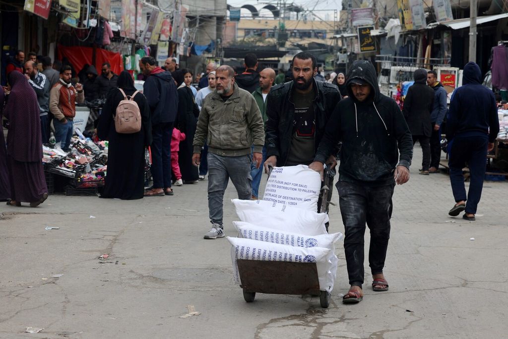 Pengungsi Palestina mendorong gerobak berisi kantong tepung terigu yang mereka terima dari Badan Bantuan dan Pekerjaan PBB untuk Pengungsi Palestina (UNRWA) di Rafah, Jalur Gaza selatan, Minggu (28/1/2024). 