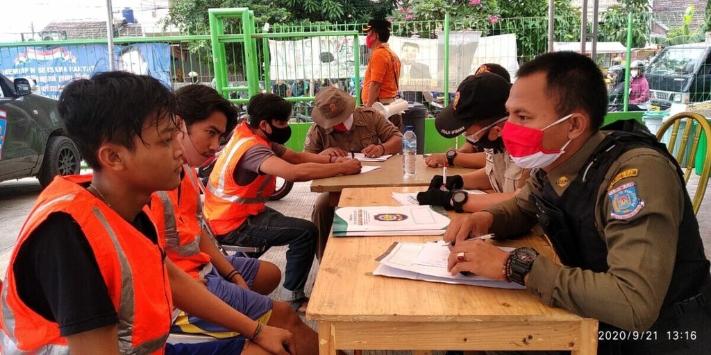 Anggota Satuan Polisi Pamong Praja (Satpol PP) Kota Tangerang Selatan, mencatat warga yang melanggar protokol kesehatan di Pasar Ceger, Tangerang Selatan, Banten, Senin (21/9/2020).
